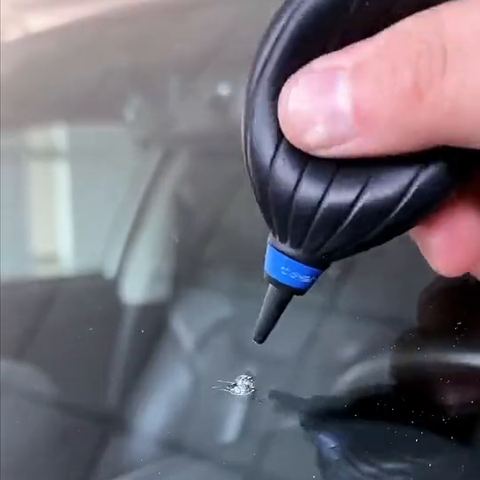 A hand blower clearing dust from a windscreen chip
